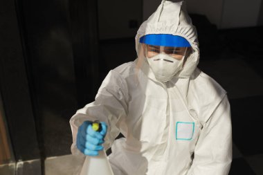 Koruyucu elbise giyen, dezenfeksiyon, temizlik, gölge ve güneş ışığı görüntüsü sırasında kimyasalları evin içine püskürten kadın işçilerin ön manzara portresi.