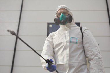 Koruyucu giysiler giyen bir işçinin düşük açılı portresi ve dezenfeksiyon ya da temizlik sırasında kimyasalları dışarı püskürtmek, boşluğu kopyalamak
