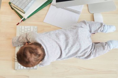 Ev işyerindeki masanın üstünde emekleyen küçük şirin bir bebeğin portresi, ev konsepti üzerine çalışan bir ebeveyn.