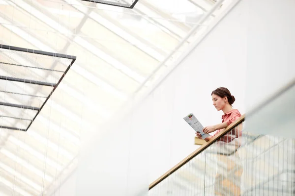 Wide angle view at young businesswoman standing on balcony and reading document in minimal office building interior, copy space