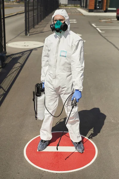 男工穿着防护服 手持消毒剂 站在室外阳光照射下的Stop标志上的垂直全长肖像 — 图库照片