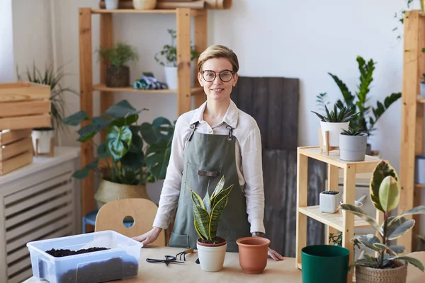 植物や土で木製のテーブルに立っている間 カメラで微笑む現代の若い女性のウエストアップ肖像画は ポット 家庭菜園のコンセプト コピースペースの準備ができて — ストック写真