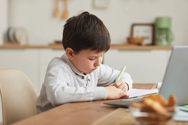 居心地の良いインテリアで自宅で勉強しながらノートに書くかわいい男の子の暖かいトーンの肖像画 コピースペース — ストック写真