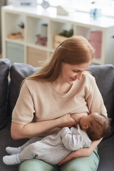 幸せな成熟した母の授乳中の赤ちゃんの垂直肖像画ながら ソファの上に家の中で座って コピースペース — ストック写真