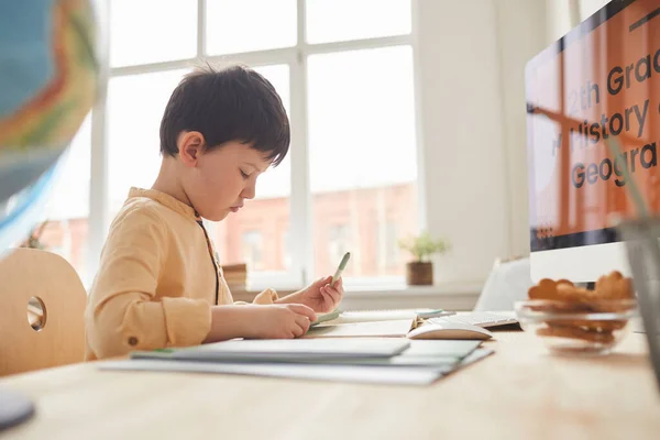 サイドビューの肖像画かわいい男の子が宿題をしながら オンライン学校のウェブサイト コピースペースとコンピュータで机に座って — ストック写真