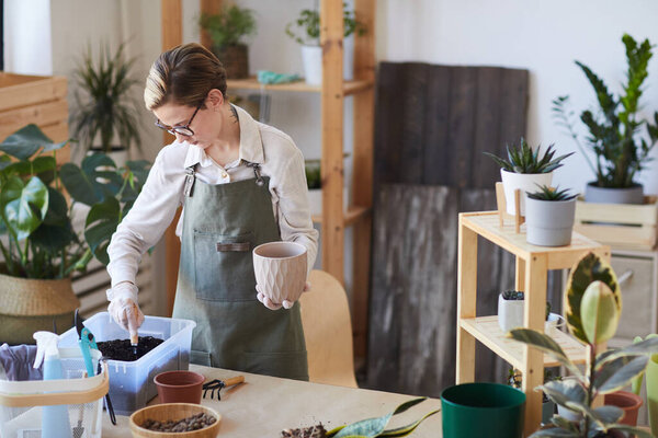 Портрет современной молодой женщины, помещающей свежую почву в цветочные горшки, наслаждаясь домашним садоводством, копировальным пространством