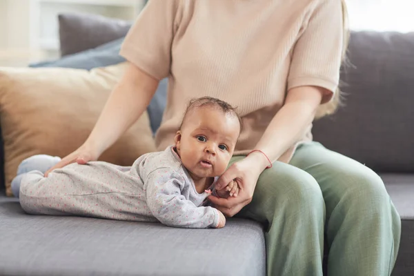 与无法辨认的白人母亲在沙发上爬行时看着相机的可爱混血婴儿的肖像 复制空间 — 图库照片