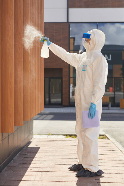 Вид сбоку портрет одного рабочего, распыляющего химикаты над зданием во время дезинфекции или очистки