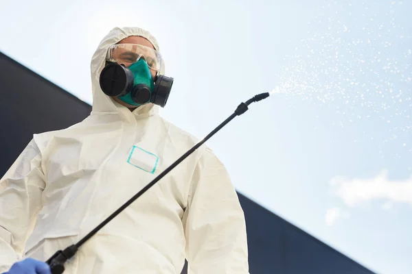 男工穿着防护服 手持消毒器 在室外喷洒化学品 站在天空背景下的低角度肖像 复制空间 — 图库照片