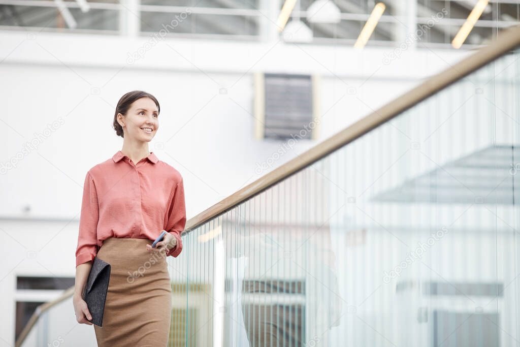 Waist up portrait of smiling businesswoman walking towards camera in contemporary office building interior, copy space