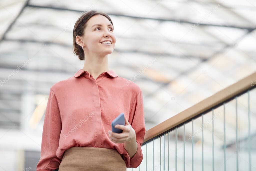 Low angle portrait of smiling young businesswoman looking away while walking towards camera in contemporary office building interior, copy space