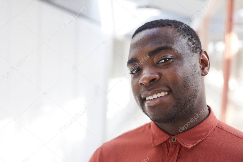 Head and shoulders portrait of contemporary African-American man looking at camera and smiling while posing in office against white background, copy space