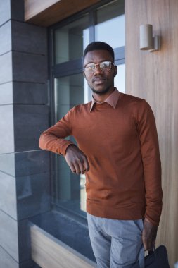 Gözlüklü Afrikalı bir işadamının dikey portresi ve ofis binasının yanında dururken kameraya bakması.