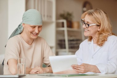 Gülümseyen kel kadının sıcak tonlu portresi. Kadın doktoru dinliyor. Alopecia ve kanser tedavisi için yapılan muayenede negatif test sonuçları gösteriyor.