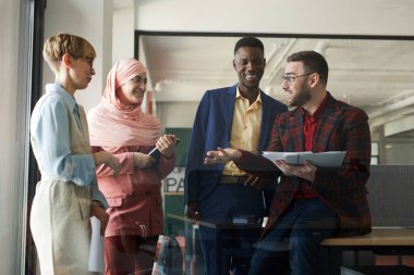 Modern çok ırklı iş adamlarının belden yukarı portresi. Etkin bir şekilde birbirleriyle konuşuyorlar ve ofiste dururken el kol hareketi yapıyorlar.