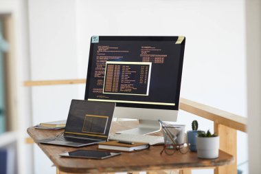 Bilgisayar ekranındaki siyah ve turuncu programlama kodunun arkaplan resmi ve modern beyaz ofis içi dijital cihazlar, boşluğu kopyala