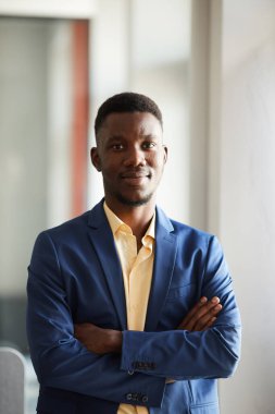 Zarif Afrikalı işadamının dikey portresi kameraya bakarken modern ofis içinde kolları çaprazlanmış bir şekilde poz veriyor.