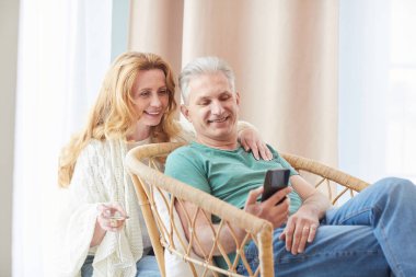 Evde dinlenirken akıllı telefon ekranına bakan zarif olgun bir çiftin sıcak tonlu portresi. Boşluğu kopyala.