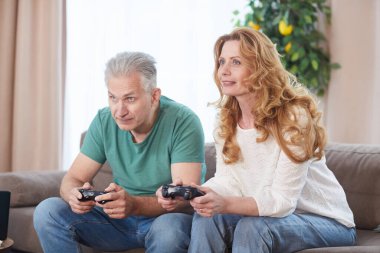 Modern olgun çiftin portresi konsol ile video oyunları oynuyor ve evde eğlenirken kontrolörleri tutuyor