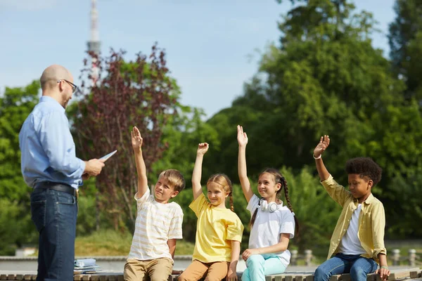 Багатоетнічна Група Веселих Дітей Які Піднімають Руки Слухають Вчителя Чоловіка — стокове фото