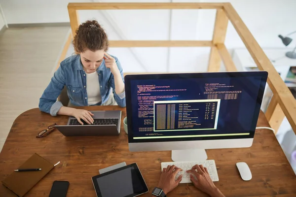在电脑屏幕上有无法辨认的男性同事的软件开发机构的办公桌前工作时 使用笔记本电脑的年轻女性的高角肖像 复制空间 — 图库照片