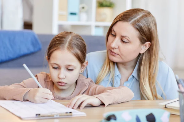 一个充满爱心的成年妈妈在舒适的室内环境中看着可爱的小女孩做作业或考试的画像 — 图库照片