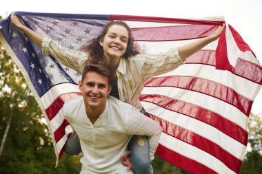 Amerikan bayrağını sallarken kameraya bakan kaygısız genç bir çiftin düşük açılı portresi.
