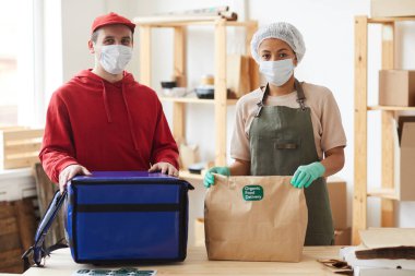 Maske takan ve kameraya bakan iki işçinin belden yukarı portresi. Ulaşılmaz yemek dağıtım servisinde paket siparişleri, kopyalama alanı.