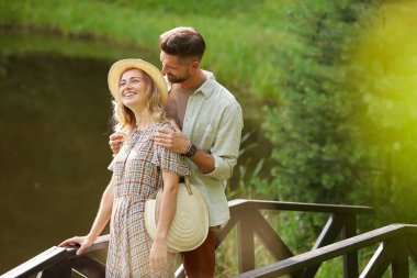 Romantik yetişkin bir çiftin portresi, ahşap köprüde, köy manzarasında yürürken mutlu bir şekilde gülümsüyor.