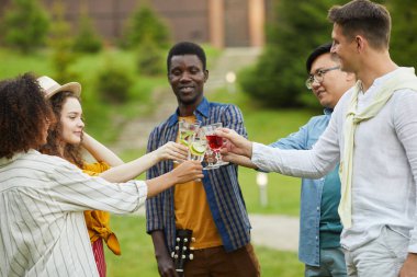 Çok ırklı bir grup insan yaz aylarında açık hava partisinin tadını çıkarırken kokteyl bardaklarını tokuşturuyor ve kadeh kaldırıyor.