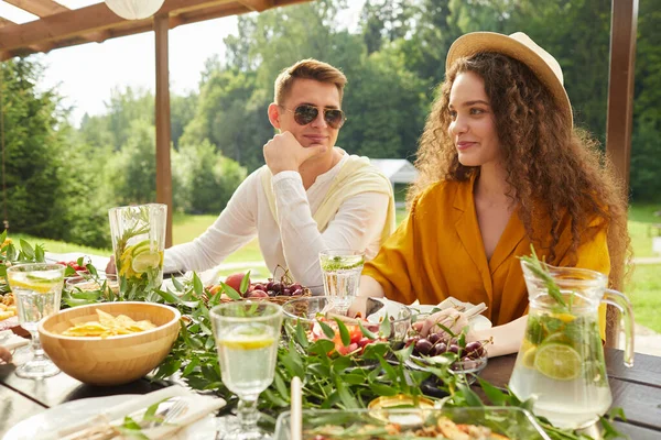 Açık havada masada otururken arkadaşlarıyla yemek yiyen genç bir çiftin renkli portresi.
