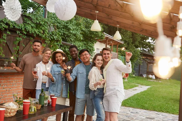 Çok ırklı bir arkadaş grubu kameraya bakıyor ve ellerinde maytap tutarken dışarıda yaz partisinin tadını çıkarıyor, mekanı kopyalıyor.