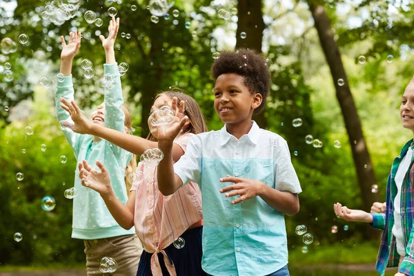 アフリカ系アメリカ人の少年と公園で遊んでいる屈託のない子供たちのグループのウエストアップの肖像画屋外で泡と遊ぶ — ストック写真