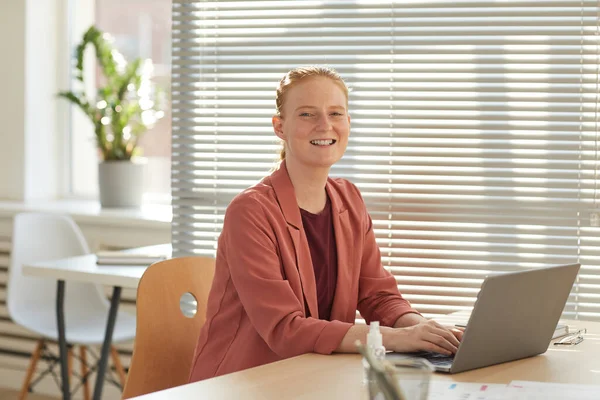 オフィスのデスクでノートパソコンを使用している間にカメラで笑顔若い赤い髪のビジネスマンの女性の候補の肖像画 コピースペース — ストック写真