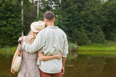 Romantik yetişkin çiftlerin arka plan portresi, kırsal alanda göl kenarında dururken kucaklaşmaları, fotokopi çekmeleri.