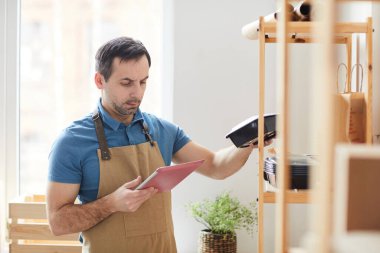 Yemek dağıtım servisinde envanter çıkartırken önlük takan olgun bir adamın belden yukarı portresi.