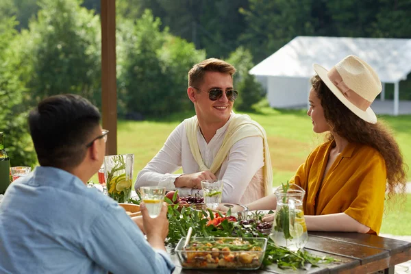 Gülümseyen genç çiftin renkli portresi. Yaz partisinde arkadaşlarıyla dışarıda yemek yerken birbirleriyle konuşuyorlar.