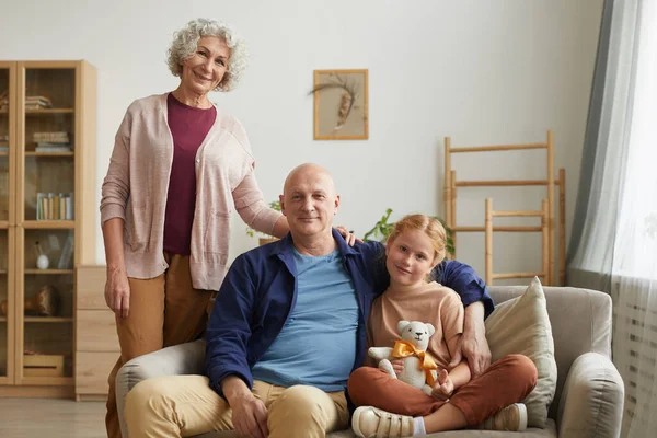 Kameraya gülümseyen modern yaşlı çiftin portresi. Evin içinde sevimli kızıl saçlı bir kızla poz verirken.