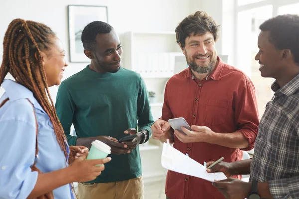 Waist up portrait of multi-ethnic group of people dressed in casual wear and smiling cheerfully while discussing work standing in office