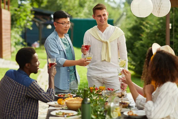민족의 친구들이 파티에서 식사를 즐기며 테이블에 기다리고 남자가 건배하는 집중하고 — 스톡 사진