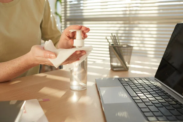 Close up pf unrecognizable woman sanitizing hands while working at desk in post pandemic office lit by sunlight, copy space