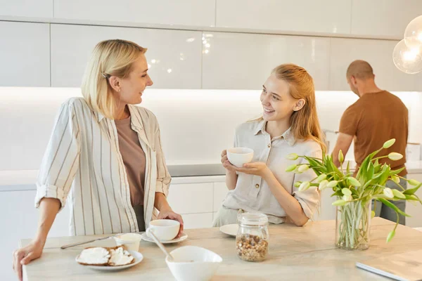 Mutfaktaki modern mutlu ailenin sıcak tonlu portresi, gülümseyen anneye odaklan kahvaltıdan zevk alırken genç kızıyla konuş, boşluğu kopyala