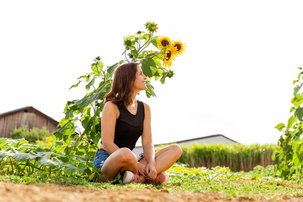 Young woman sitting laughing under a sunflower in the sunlight.