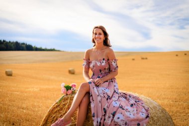 Yaz aylarında genç kadın bir saman balya çiçekli oturan elbise ve rüzgar estigi saçları sağlar.