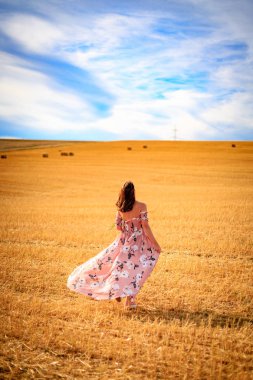 Yaz elbisesinin rüzgar iken genç kadın anız alanın üzerine yürür.