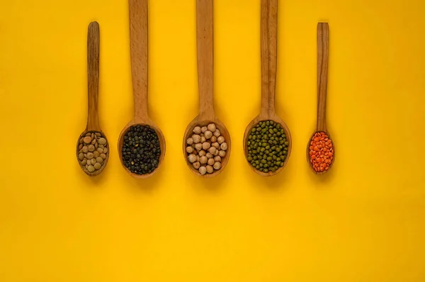 Ξύλινα κουτάλια και συστατικά σε κίτρινο φόντο. Η έννοια της βιολογικά προϊόντα σιτηρών, υγιεινή διατροφή, την επιλογή των καθαρά τρόφιμα — Φωτογραφία Αρχείου