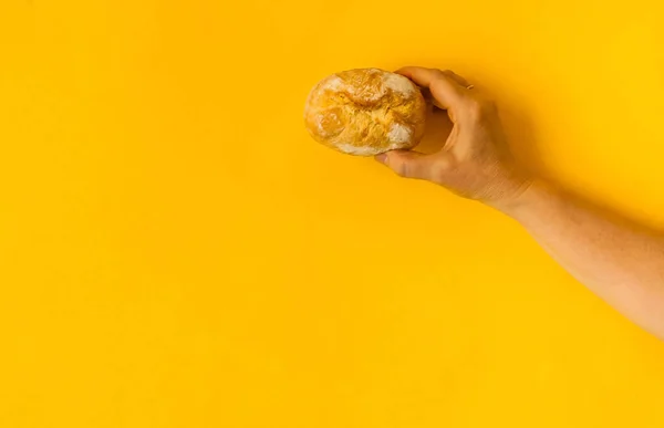 Pequeno pão de trigo fresco é realizada pela mão feminina no fundo amarelo brilhante, luz natural, espaço de cópia, close-up , — Fotografia de Stock