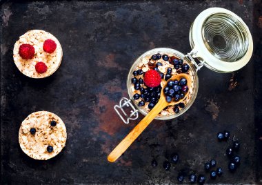 Yulaf ezmesi meyve ve fındık, sağlıklı kahvaltı malzemeler. Yaban mersini ve ahududu vintage paslı metal arka plan, organik gıda kavramı, kopya alanı, açık cam kavanoza ev yapımı granola portre