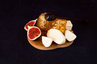 Bal ile taze incir, ahşap tahta üzerinde keçi peyniri. Koyu mavi zemin üzerine bütün ve dilimlenmiş incir yaratıcı düzeni. 