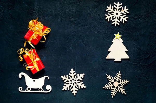Декоративные деревянные рождественские снежинки и сани. Тёмно-синий фон с рождественскими подарочными коробками, вид сверху. . — стоковое фото